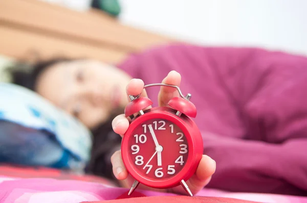 Woman snoozing a red alarm clock