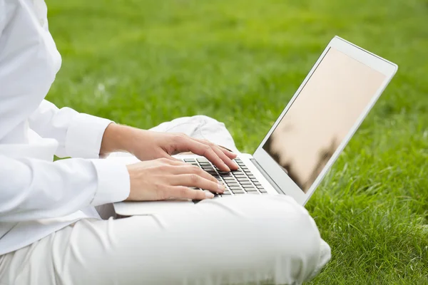 Woman hands typing on a laptop keyboard, in garden