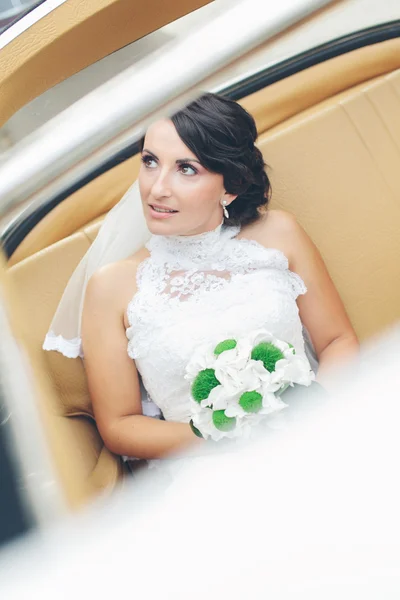 Bride in a vintage car with white dress and green bouquet
