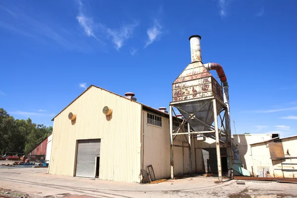 Rusted metal mining wagons standing outside an industrial warehouse with train tracks running in front of the building.