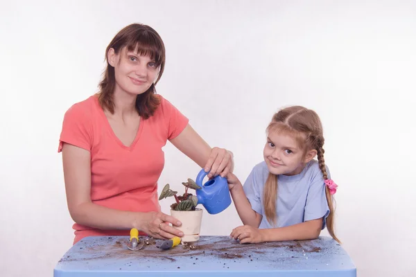 Mom and daughter watering potted flower room