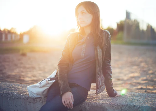 Beautiful model woman with long hair dressed in casual jeans, leather Jacket. Beauty romantic girl outdoors. Summer glow sun light . Autumn Sunset. Sunshine. Toned warm colors.