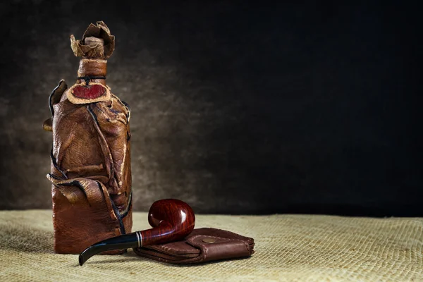 Leather vintage bottle with a pipe and a purse on a dark backgro