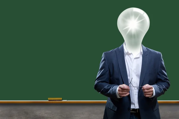 Teacher with light bulb head in front of chalk board