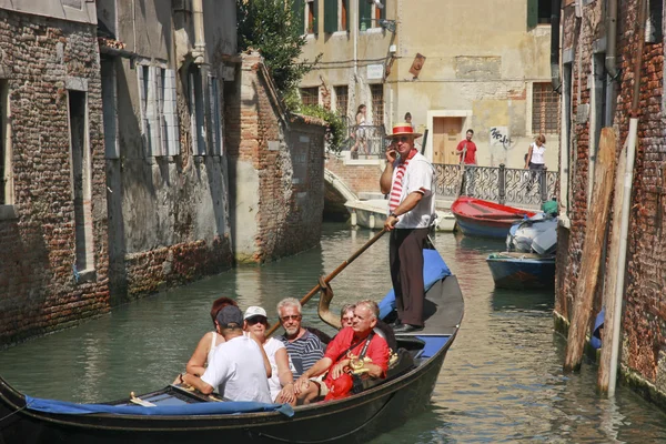 Venetian gondolier rowing gondola with passengers and speaking to somebody by cellphone