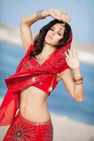 Beautiful Indian Woman in Traditional red dress and golden jewelry outdoors