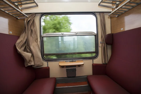 Train compartment with red seats and a view out the window