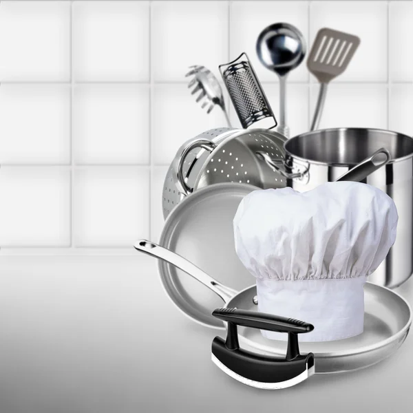 Cook cap, pile of pots and pans on the kitchen background.