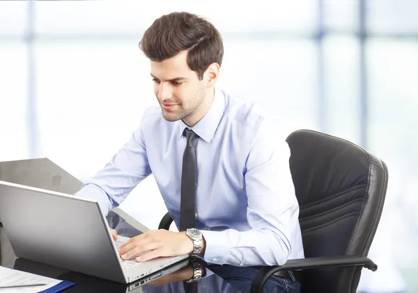 Happy young businessman using laptop in his office