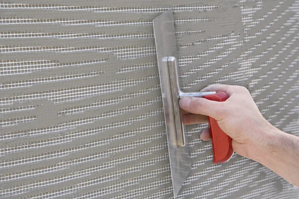 Master makes plaster on a wall with mesh and glue