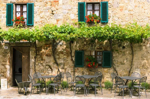 Cafe tables and chairs outside a stone building in Tuscany, Italy