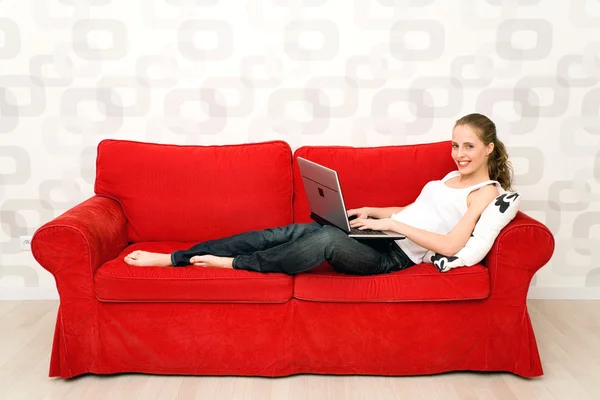 Young woman lying on couch with laptop