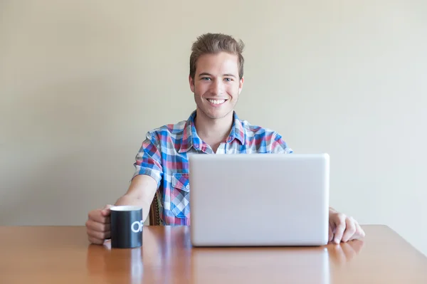 Young adult using computer and holding cup of coffee