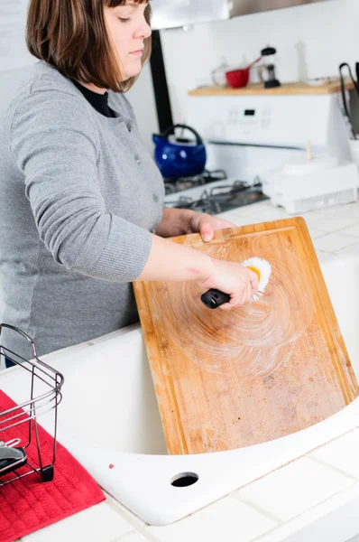 Woman washes cutting board in kitchen sink