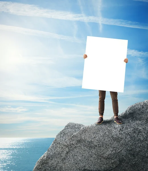 Man standing on a rock with blank poster in his hands