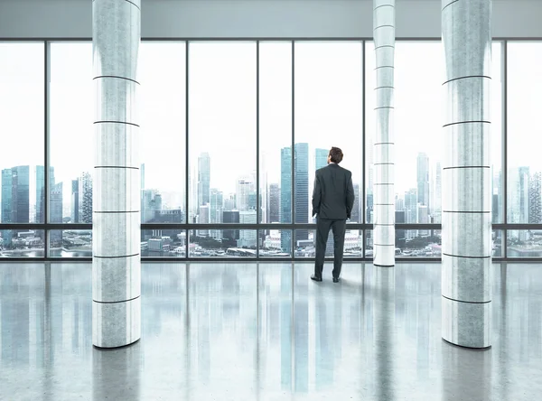 Businessman standing in large office and looking at city