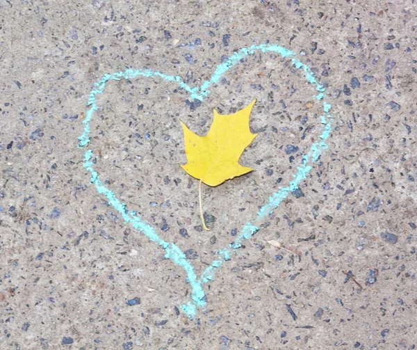 Yellow leaf in the heart drawn in chalk on gray asphalt
