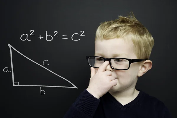 Smart young boy stood infront of a blackboard