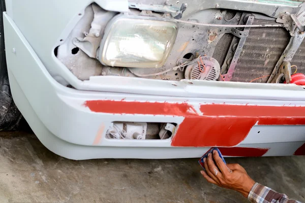 Auto mechanic preparing the front bumper of a car for painting