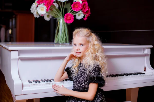Little blond girl standing near white piano