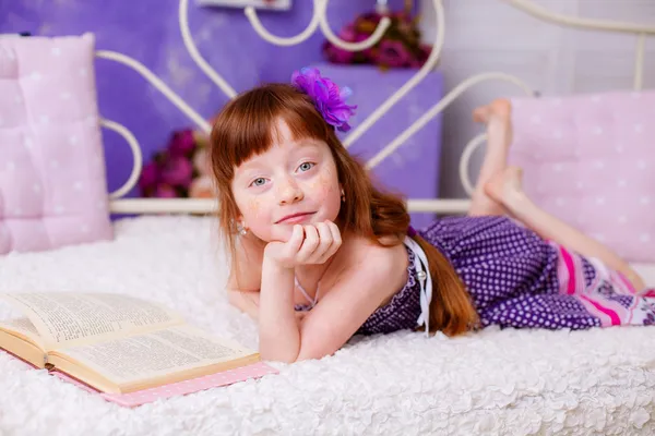 Red-haired girl reading a book on bed