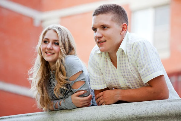 Two people standing on balcony leaning on railing