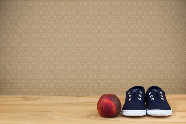 Sneakers and peach on wooden table over vintage wallpaper