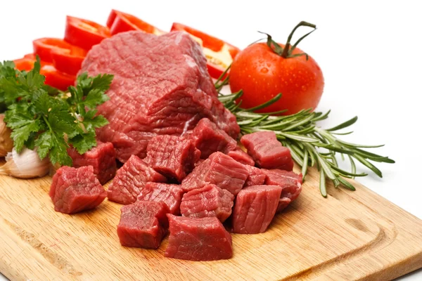 Raw fresh meat sliced in cubes on board with vegetables