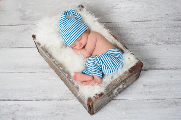 Newborn baby wearing blue and white striped pajamas and sleeping in a vintage, wooden, soda pop crate.