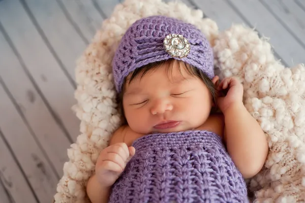 Sleeping newborn baby girl wearing a fancy, lavender flapper style crocheted hat.