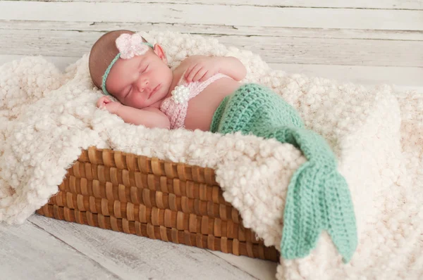 Newborn girl wearing a crocheted mermaid costume, sleeping in a basket