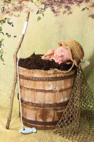 7 day old newborn baby boy sleeping in an old, weathered wooden bucket.