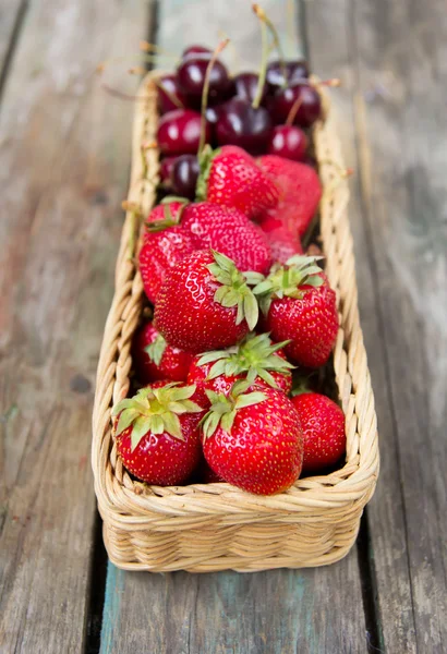 Strawberry and sweet cherry in a wattled basket on a wooden table