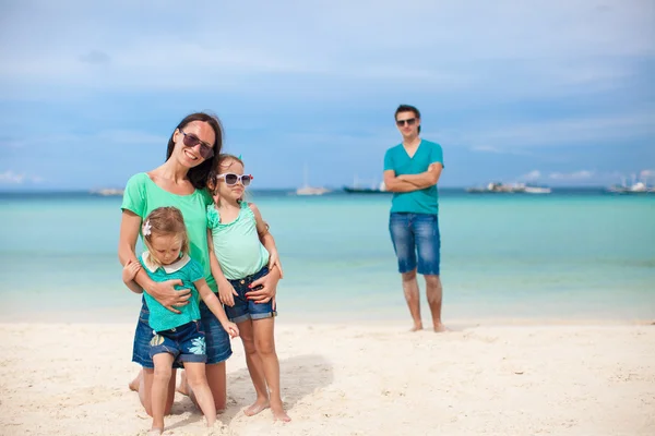 Mom with her cute daughters in the foreground and dad in the background on the beach