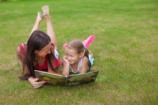 Young mother and her cute daughter reading book outdoor
