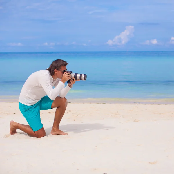 Profile of young man with camera in hand on beautiful white sandy beach