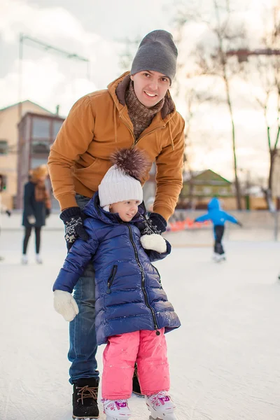 Young Dad teaches his little daughter to skate on the rink