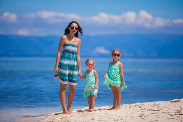 Adorable little girls and young mother walking on tropical white beach in desert island