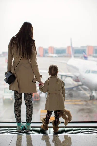 Mother and little daughter looking out the window at airport terminal
