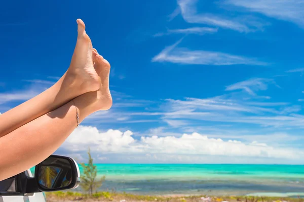 Female barefoot from the window of a car on background tropical beach