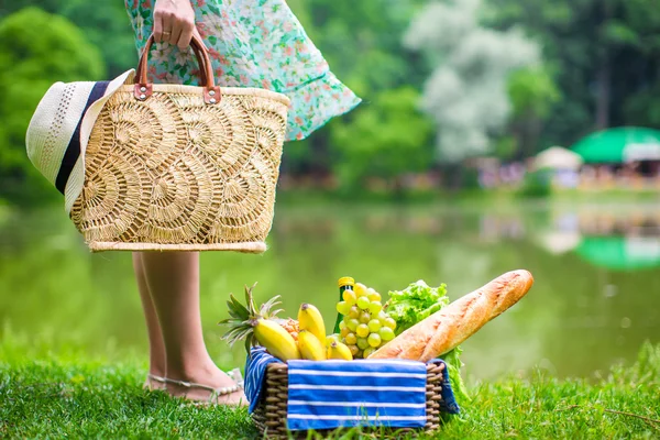 Picnic basket with fruits, bread and hat on straw bag
