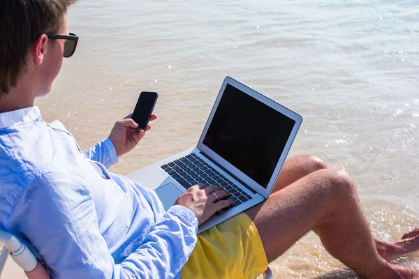Young businessman using laptop and telephone on tropical beach