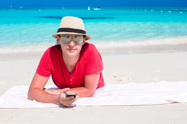 Young man with cell phone on tropical white beach