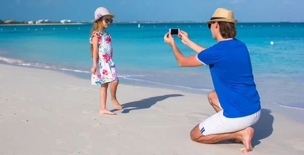 Young father making photo on phone of girl at beach