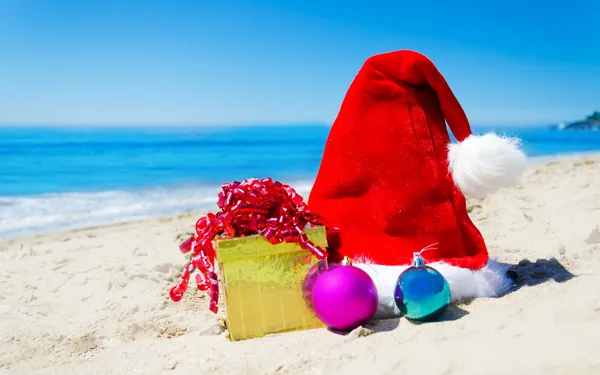 Christmas hat with gift box and christmas balls on the beach