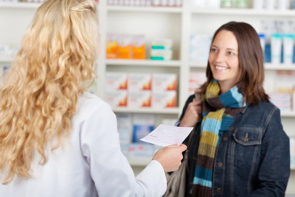 Female Customer Looking At Pharmacist Holding Prescription Paper