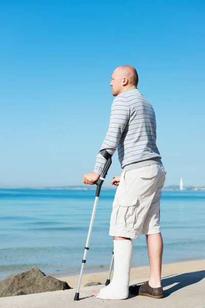 Injured Man with Crutches at sea side