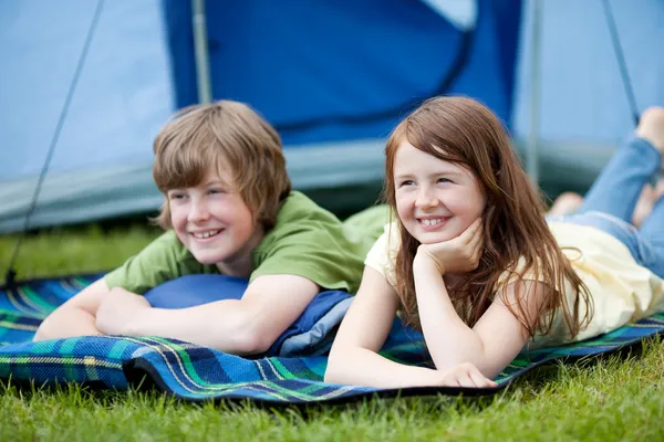 Two Kids Lying On Blanket With Tent In Background