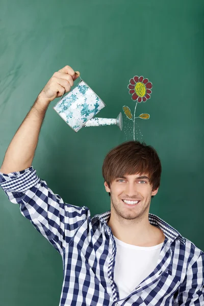 Male Student Holding Watering Can With Flower Drawn On Chalkboard