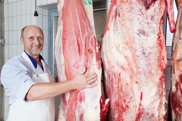 Happy butcher close to cow carcasses